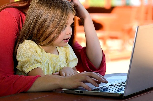 A small girl sits on the lap of a woman. They are both at a laptop watching something.