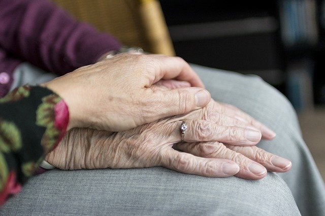 A woman's hand drapes across a folded pair of hands that belong to a much older woman. Care and consideration for an elderly relative.