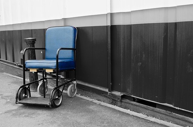 A Blue wheelchair sits alone against a gray and black wall for a background.