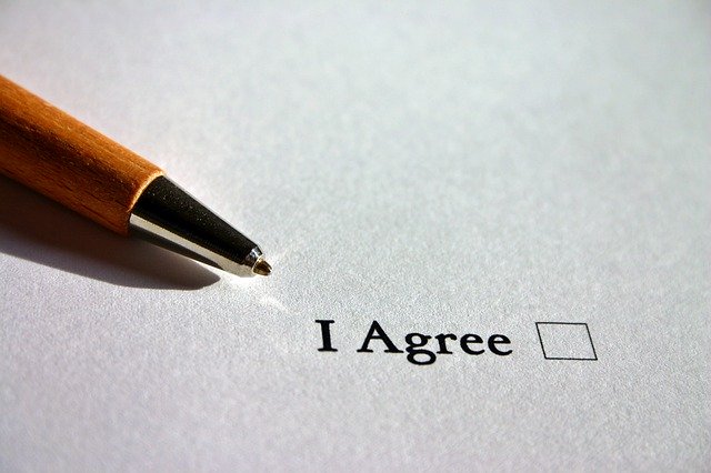 A page reads "I Agree" with an empty square beside the words. A pen awaits use to check the box.