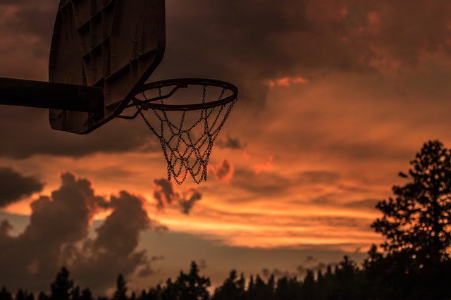 A bright orange sunset sky is the backdrop for a deserted looking basketball net.