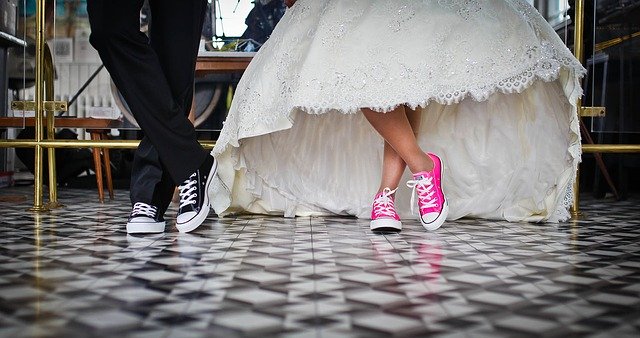 From the knees down, a bride and groom are showing off their cool sneakers. Hers are pink and his are black.